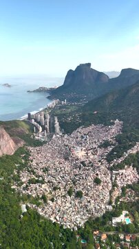 Aerial view of the dense urban landscape of Rocinha favela nestled between lush green mountains and the coastline in Rio de Janeiro, State of Rio de Janeiro, Brazil.