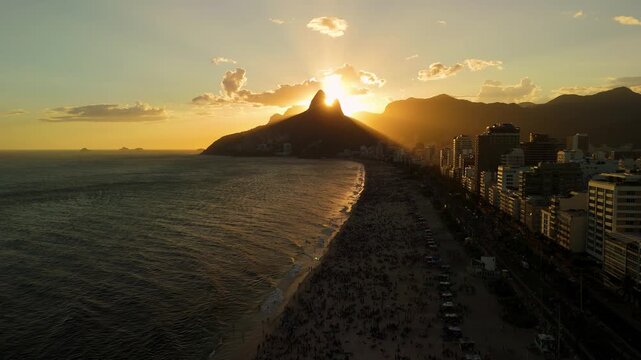 Aerial view of the sun setting behind the Dois Irmaos mountains over the coastline and city skyline of Rio de Janeiro, State of Rio de Janeiro, Brazil.