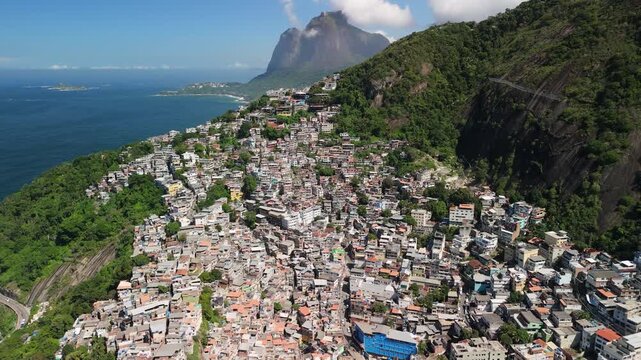Aerial view of a densely populated favela built on a steep hillside overlooking the ocean with lush green mountains in the background in Rio de Janeiro, State of Rio de Janeiro, Brazil.