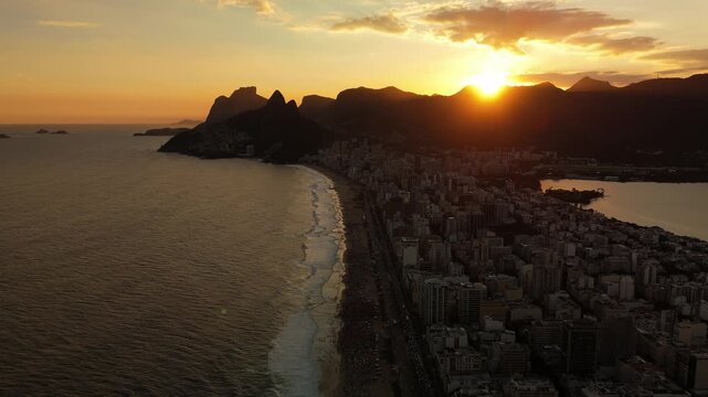 Aerial view of Ipanema beach at sunset with golden light reflecting on the ocean waves and the city skyline of Rio de Janeiro, State of Rio de Janeiro, Brazil.