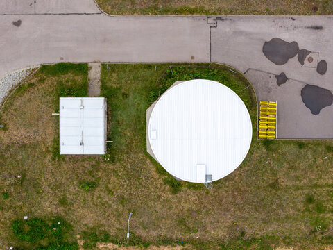 Aerial view of a circular fire protection water tank and a small utility building situated on a grassy plot next to an asphalt road in Warsaw, Masovian Voivodeship, Poland.