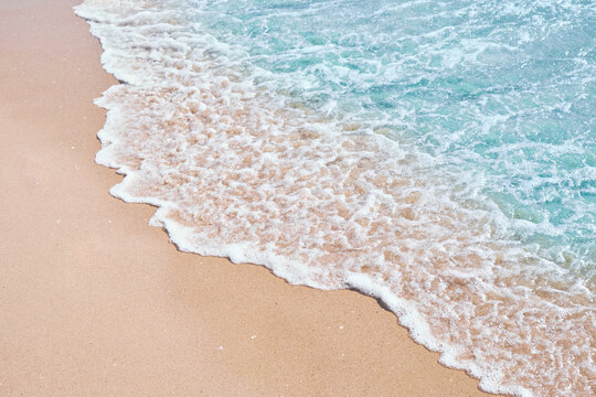 Turquoise sea wave with white foam washing over clean sandy beach, top view high angle shot