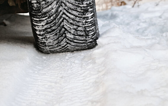 Close-up of a car winter tire with snow in the tread, showing traction pattern on a snowy road during cold weather conditions