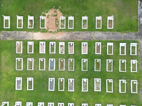 Aerial view of rows of graves in a cemetery with white rectangular borders set in green grass in Indonesia.