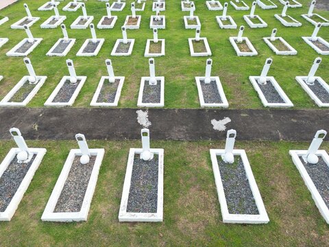 Aerial view of a hero cemetery with rows of white grave markers set in green grass in INDONESIA.