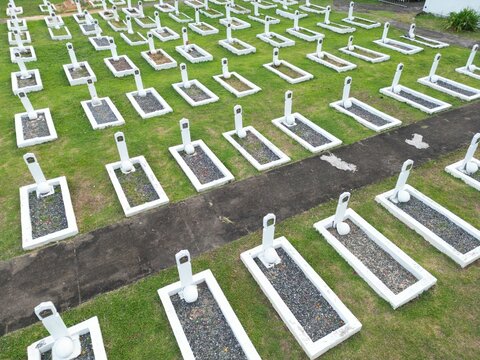 Aerial view of the Hero Cemetery featuring rows of white grave markers set in green grass with a dark paved walkway in Indonesia.