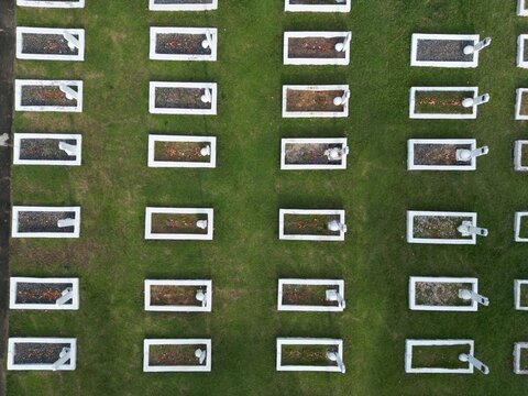 Aerial view of rows of graves in a Heroes Cemetery with white borders on green grass in INDONESIA.