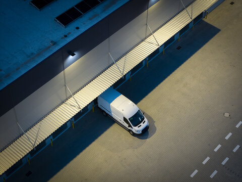 Aerial view of a white delivery van parked at a logistics hub loading dock under artificial lighting in Krakow, Lesser Poland Voivode, Poland.