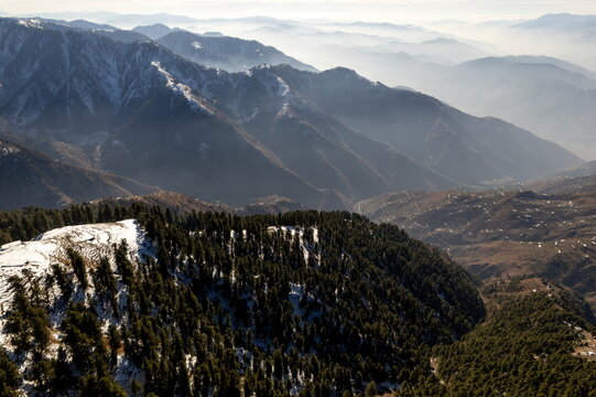 Aerial view of Pir Chinasi mountain peak covered in snow with dense pine forests and rolling hills in the background in Muzaffarabad, Azad Jammu Kashmir, Pakistan.
