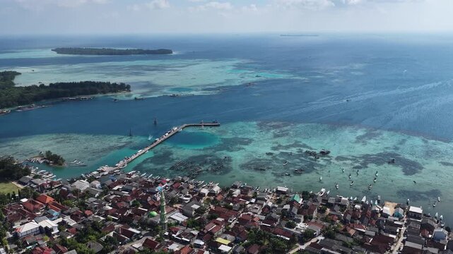 Aerial view of a coastal village with a long pier extending into turquoise waters and small boats anchored near the shore in Karimunjawa, Central Java, Indonesia.