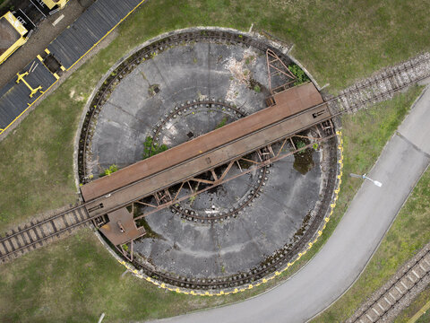 Aerial view of a historic railway turntable with rusted metal tracks and concrete base surrounded by grass and train tracks in Krakow, Lesser Poland Voivode, Poland.