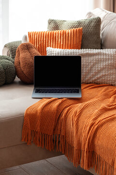 Laptop on couch with textured pillows and orange throw blanket cozy home comfort