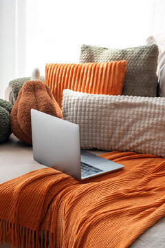 Cozy home office setup with laptop and plush autumn themed pillows and throws arranged on a sofa for comfortable remote work