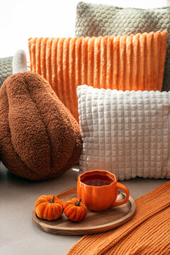 Cozy Autumn Scene with Pumpkin Decorations and Warm Beverage on Tray Surrounded by Textured Pillows and Orange Scarf