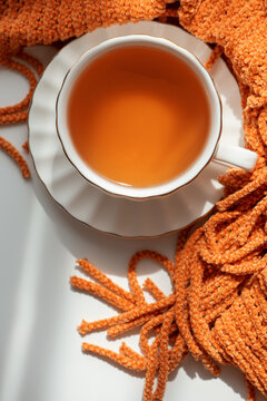 Warm cup of orange tea served in elegant porcelain cup on white saucer with soft fuzzy textile beside it creating cozy atmosphere warm beverage refreshment comfort