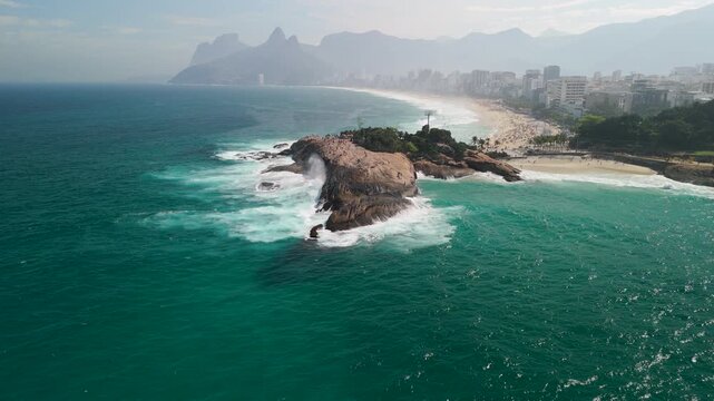 Aerial view of Arpoador rock formation surrounded by turquoise ocean waves and sandy coastline in Rio de Janeiro, Rio de Janeiro, Brazil.