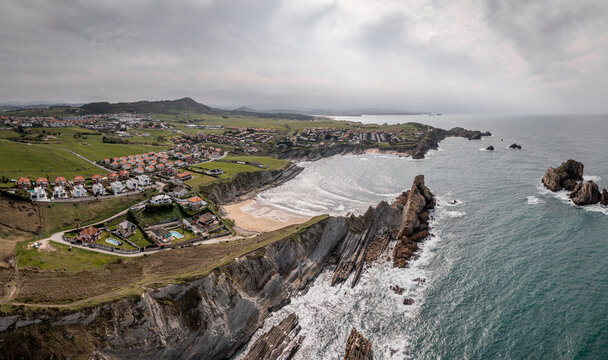 Aerial view of Arnia Beach with its dramatic rock formations, sandy shoreline, and surrounding residential area in Cantabria, Spain.