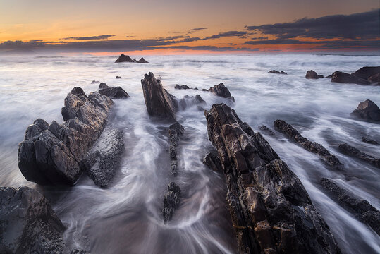 Stunning long exposure sunset at Barrika beach showing silk water flowing between geological flysch rock formations on the Basque coast of Spain