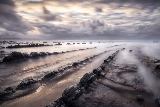 Stunning long exposure sunset at Barrika beach showing silk water flowing between geological flysch rock formations on the Basque coast of Spain