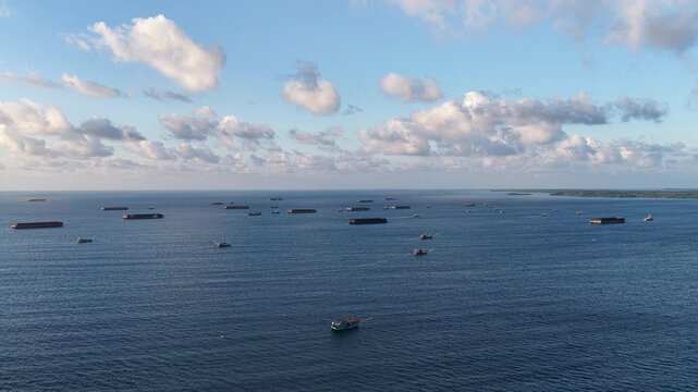 Aerial view of cargo barges scattered across the open sea with a small fishing boat in the foreground under a clear sky in Karimunjawa, Central Java, Indonesia.