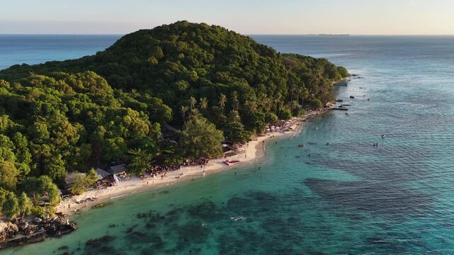 Aerial view of a tropical island beach with lush green forest, white sand, and turquoise water in Karimunjawa, Central Java, Indonesia.