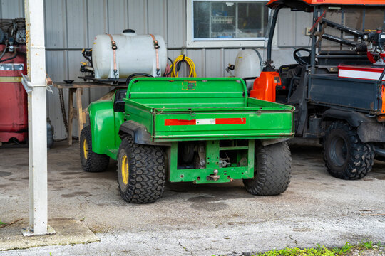 Green utility vehicle or golf cart bed parked inside a farm garage near an air compressor, water tank, and off-road machinery.