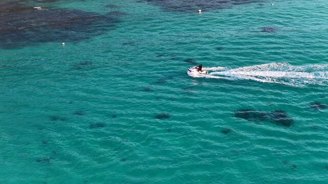 Aerial view of a person riding a jet ski on the clear turquoise water of the sea in Karimunjawa, Central Java, Indonesia.