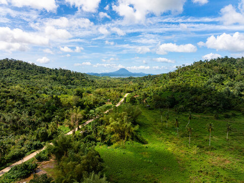 Aerial view of Mount Capuas rising above lush green hills and a winding dirt road through the tropical landscape of Taytay, Mimaropa, Philippines.