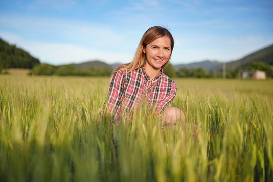 Young woman wearing a shirt crouching in unripe green wheat field, smiling