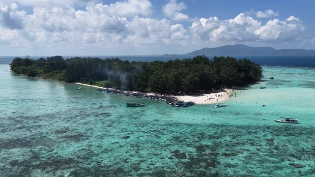 Aerial view of a tropical island surrounded by turquoise waters and coral reefs, with numerous small boats moored along the white sandy beach in Karimunjawa, Central Java, Indonesia.