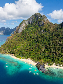Aerial view of Seven Commandos Beach with turquoise waters, limestone cliffs, and traditional outrigger boats anchored near the shore in El Nido, Palawan, Philippines.