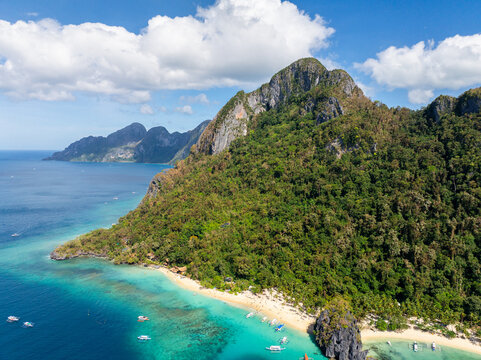 Aerial view of Seven Commandos Beach with turquoise water, white sand, lush green limestone cliffs, and small boats in El Nido, Palawan, Philippines.