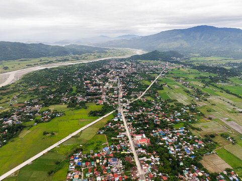 Aerial view of the town surrounded by lush green rice fields and mountains in the distance, with a main road running through the urban area in Bayombong, Cagayan Valley, Philippines.