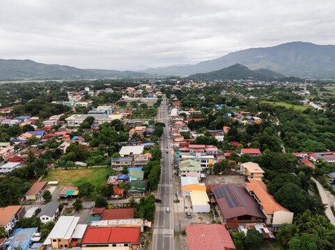 Aerial view of Bayombong town with a central road, residential buildings, lush greenery, and distant mountains under a cloudy sky in Bayombong, Cagayan Valley, Philippines.
