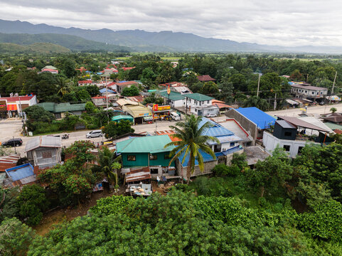 Aerial view of Bayombong town featuring residential houses, lush tropical trees, and local roads nestled against a backdrop of mountains in Bayombong, Cagayan Valley, Philippines.