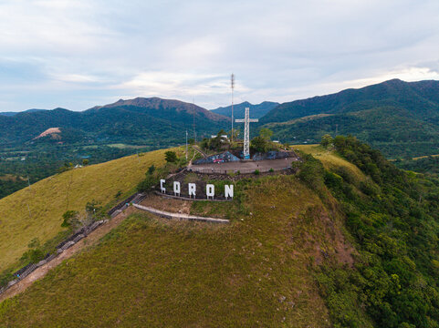 Aerial view of Mount Tapyas Viewdeck with its iconic giant cross and large Coron sign set atop a grassy hill overlooking the surrounding mountains in Coron, Mimaropa, Philippines.