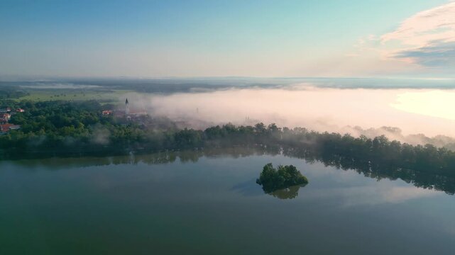 Aerial view of Svet Pond surrounded by trees and morning mist in Trebon, Jihocesky kraj, Czechia.