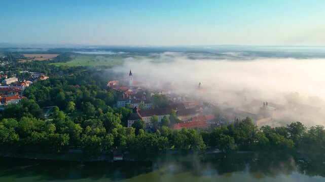 Aerial view of Svet Pond and historic rooftops of Trebon surrounded by morning mist in Trebon, Jihocesky kraj, Czechia.