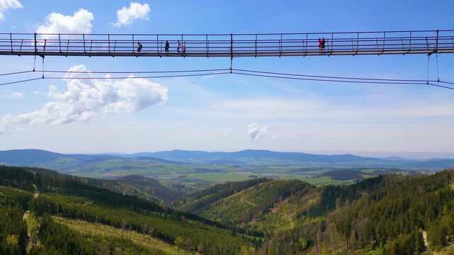 Aerial view of the lush green forested hills and rolling mountains under a bright blue sky in Dolni Morava, Pardubicky kraj, Czechia.