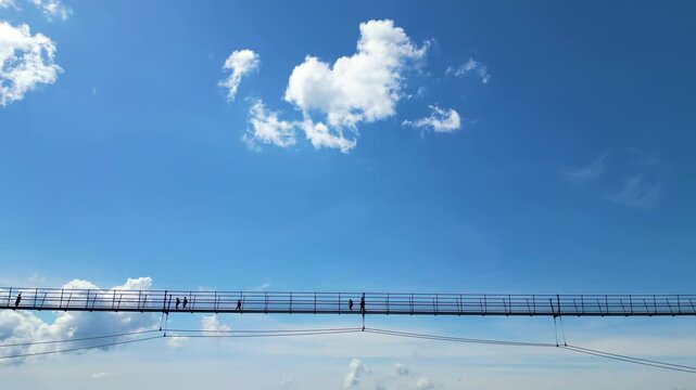 Aerial view of Sky Bridge 721 with people walking across the suspension bridge against a bright blue sky in Dolni Morava, Pardubicky kraj, Czechia.