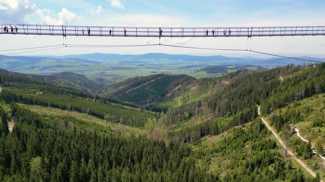 Aerial view of Sky Bridge 721 with people walking across the suspension bridge above a lush green valley and dense forest in Dolni Morava, Pardubicky kraj, Czechia.