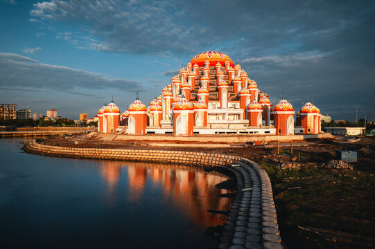 Aerial view of Masjid Kubah 99 Asmaul Husna with its orange and white domes reflecting in calm water under a dramatic sky in Kecamatan Mariso, Sulawesi Selatan, Indonesia.