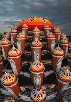 Aerial view of Masjid Kubah 99 Asmaul Husna featuring its distinctive orange and yellow tiled domes under a dramatic sky in Kecamatan Mariso, Sulawesi Selatan, Indonesia.
