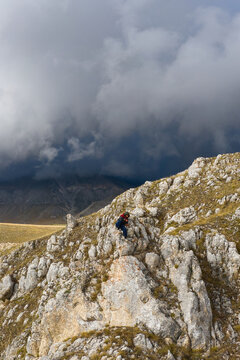 Aerial view of a person sitting on the rocky terrain of Campo Imperatore with dramatic storm clouds gathering over the mountains in L'Aquila, Abruzzo, Italy.