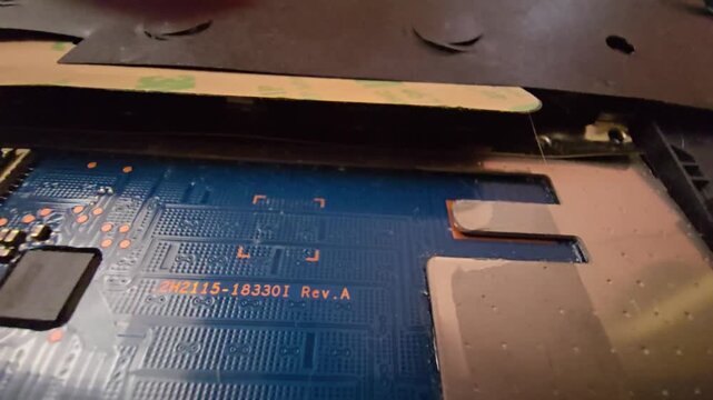 Close-up macro footage of the internal components, blue circuit board, and revision code inside a dismantled laptop or electronic device, highlighting  computer hardware and technology maintence