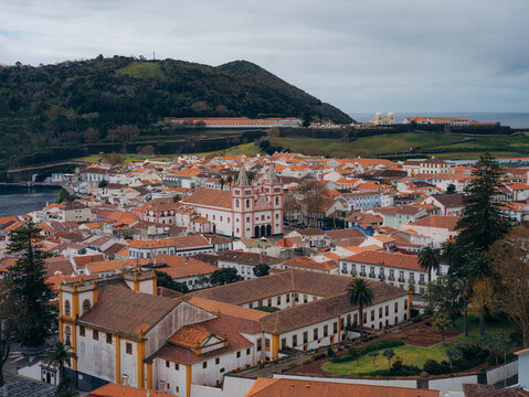 View of the historic center with its traditional red-tiled rooftops, the prominent cathedral, and surrounding lush hills in Angra do Heroismo, Azores, Portugal.