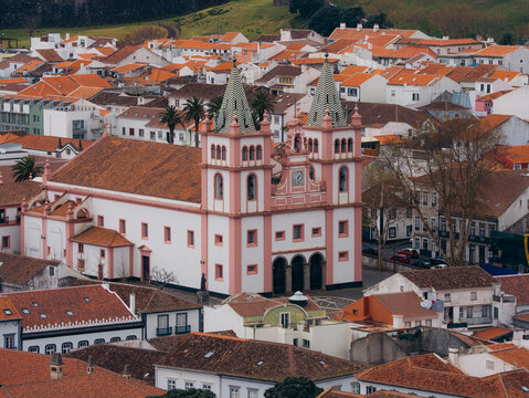 View of the historic Cathedral of Angra do Heroismo with its distinctive twin towers and pink facade, surrounded by traditional terracotta-roofed houses in Angra do Heroismo, Azores, Portugal.