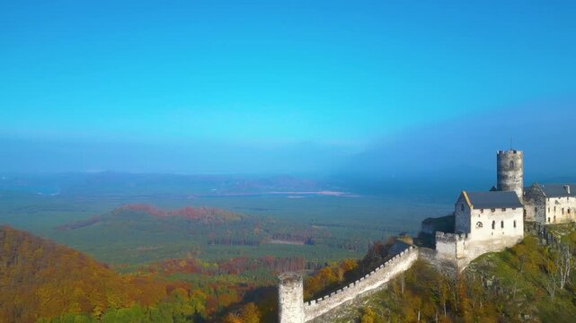 Aerial view of State Castle Bezdez with stone walls and towers overlooking the autumn forest landscape under a clear blue sky in Bezdez, Liberecky kraj, Czechia.