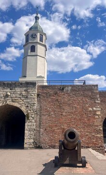 View of the historic Sahat Kula clock tower and a vintage cannon at the Belgrade Fortress under a bright blue sky in Belgrade, Serbia.