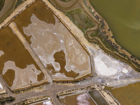 Aerial view of salt pans with textured saline pools, earthen embankments, and a pile of harvested sea salt in Moncarapacho, Faro District, Portugal.
